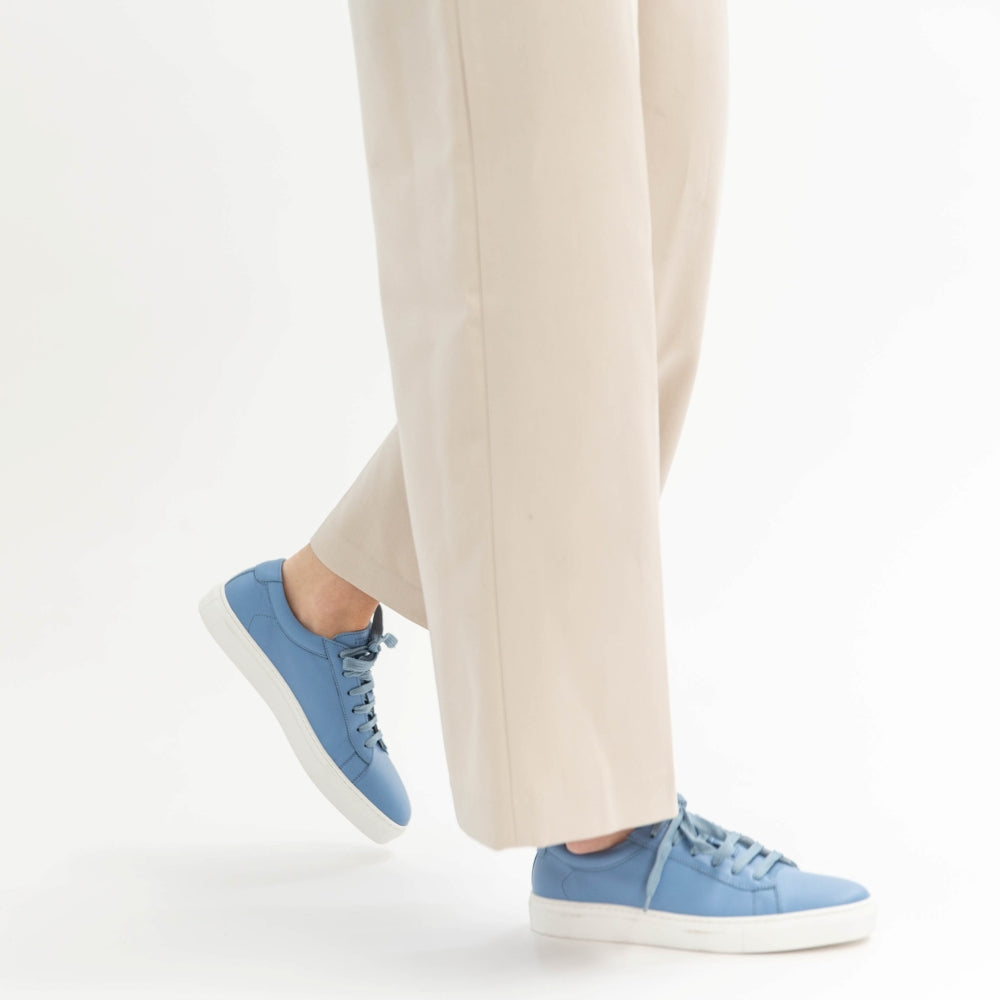 Blue sneakers worn with beige pants on a white background