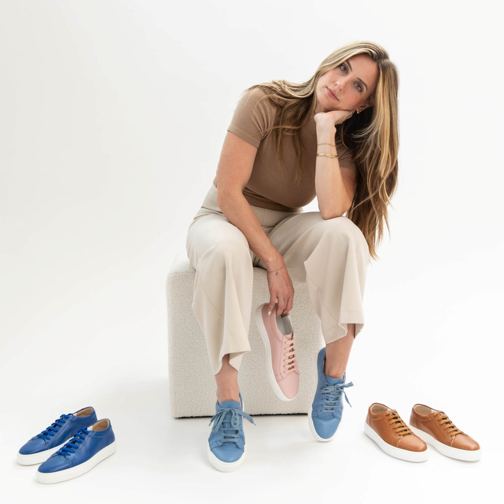 Woman sitting on a chair with various colored sneakers displayed around her.