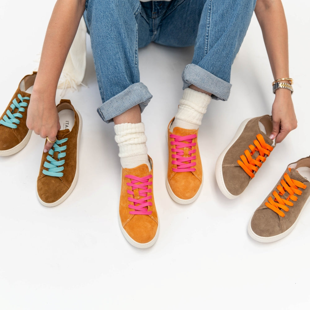 Person wearing colorful sneakers with different colored laces on a white background
