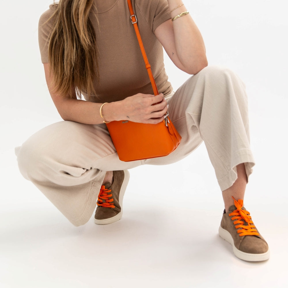 Person squatting and holding an orange handbag on a white background