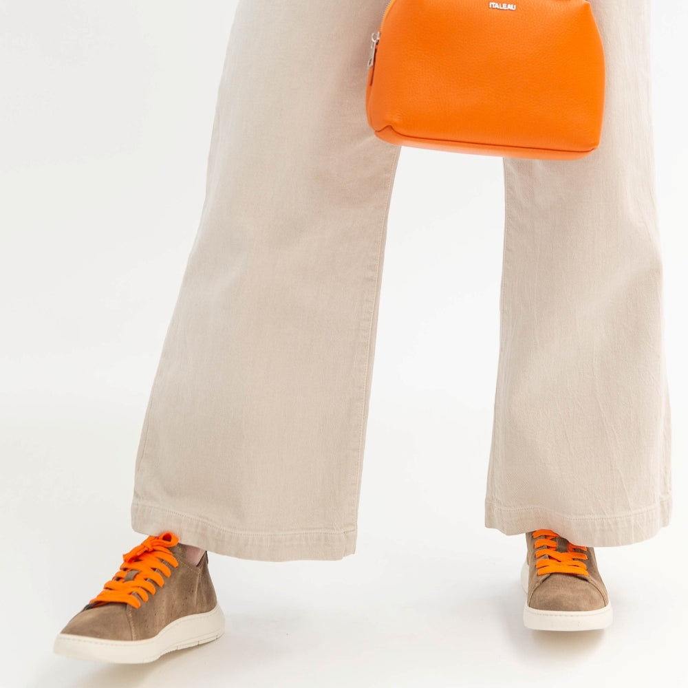 Person wearing beige pants and brown shoes with orange laces, carrying an orange bag on a white background